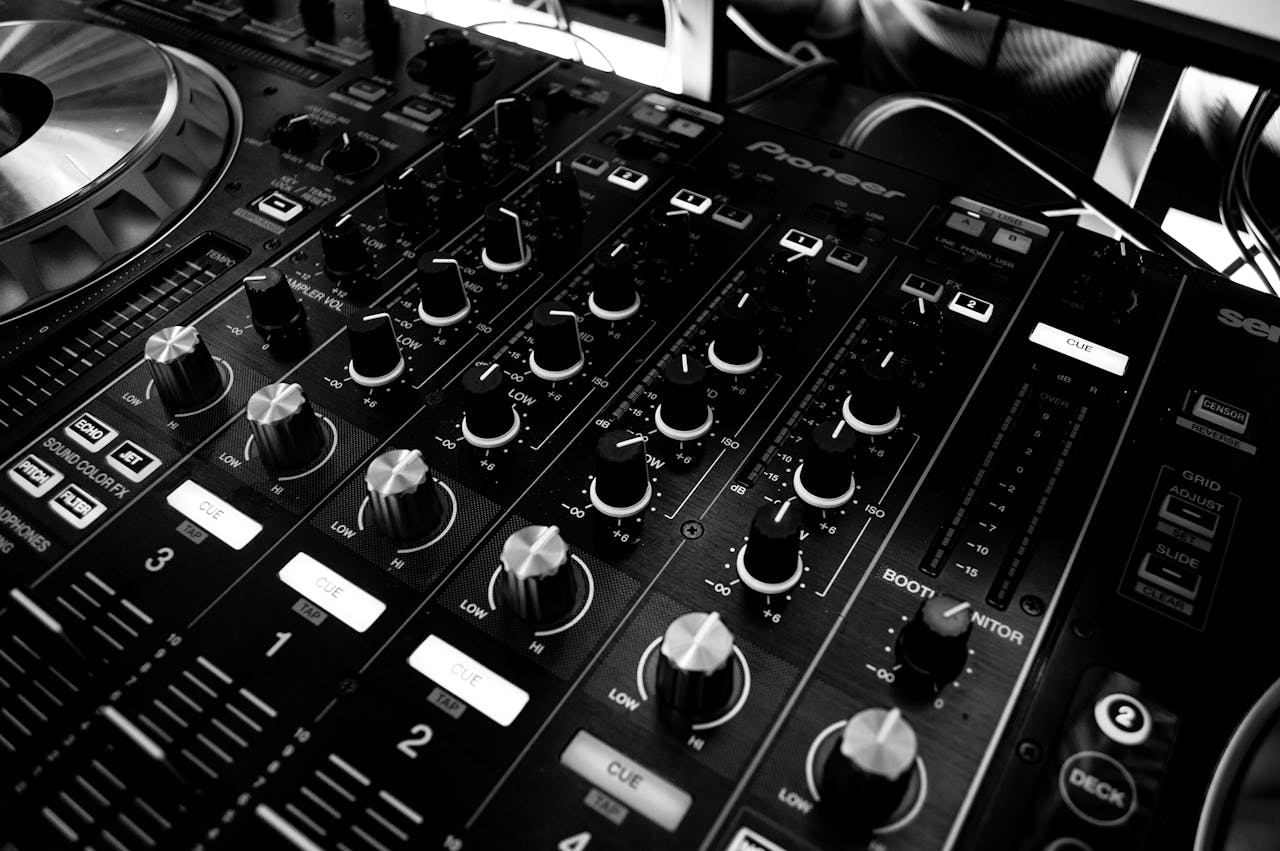 about-us Black and white close-up of a DJ's audio mixing console with knobs and controls.